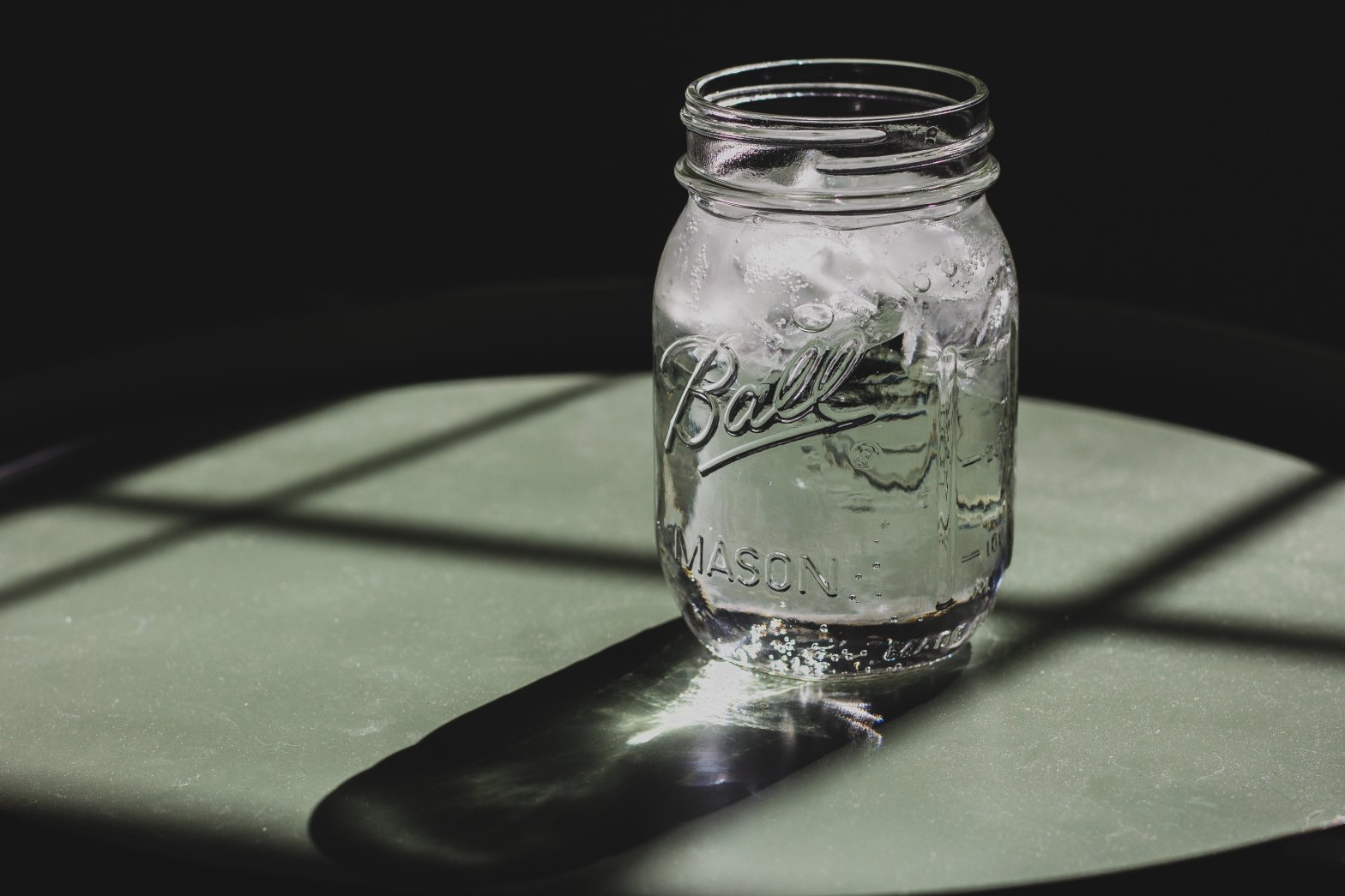 Mason jar of water with ice on a table in the sunlight falling through a paned glass window